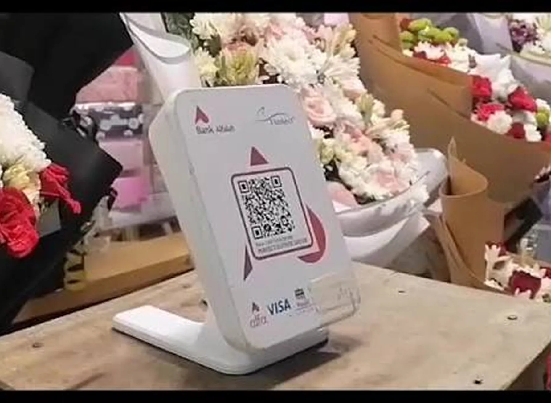 Bank Alfalah QR payment stand displaying a Visa/Mastercard QR code among a florist's bouquets